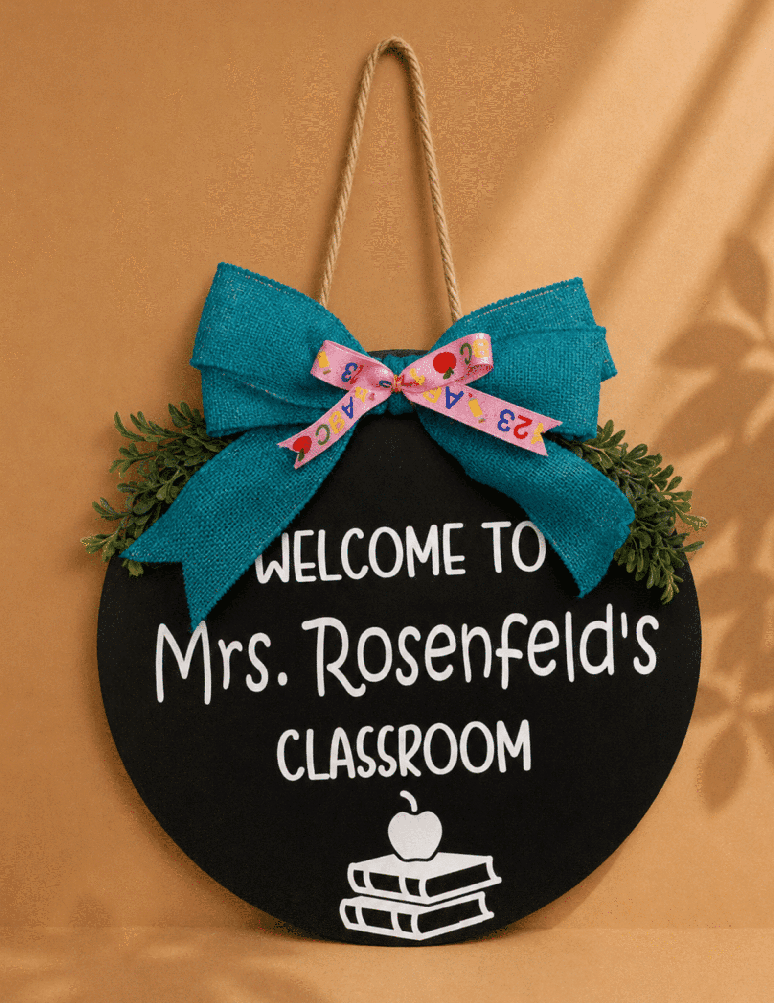 Personalized round teacher classroom door sign with custom name, greenery, and decorative bow.