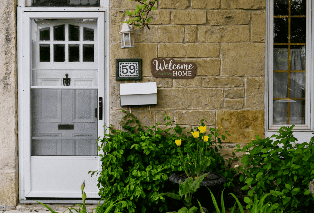 Personalized "Welcome Home" wooden sign mounted beside a house number on a stone exterior entryway.