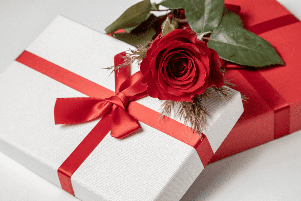 Elegant wedding gift boxes wrapped with red ribbons and topped with a red rose, representing thoughtful personalized wedding gifts for newlyweds.