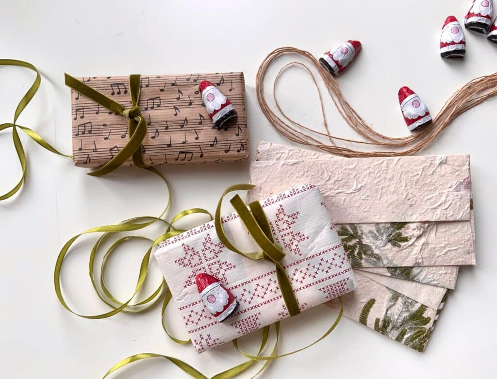 Wrapped Secret Santa gifts in patterned paper with velvet ribbon, twine, and mini chocolate Santa figures